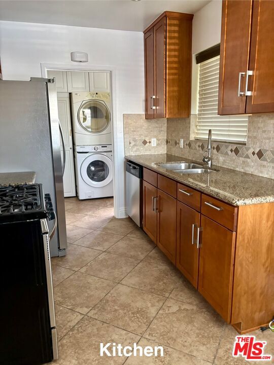 kitchen featuring sink, backsplash, light stone countertops, stacked washer and dryer, and appliances with stainless steel finishes