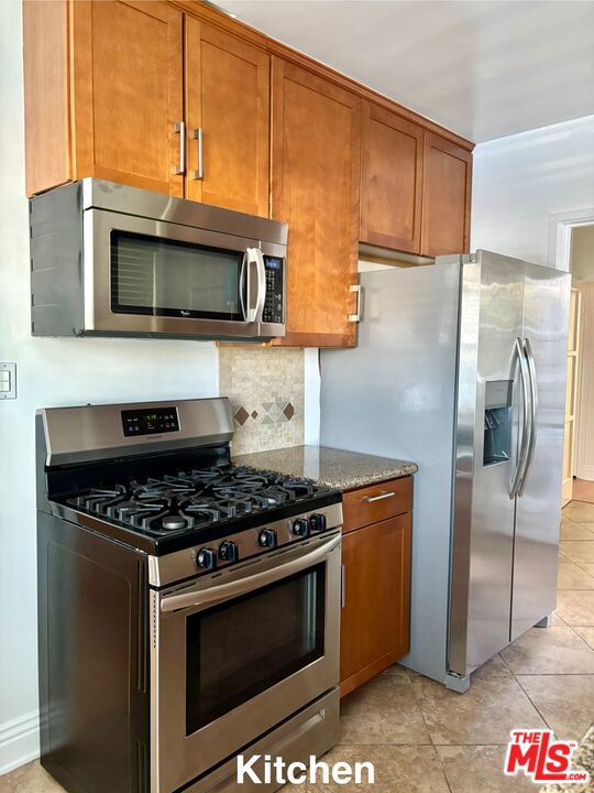 kitchen with stainless steel appliances, stone countertops, light tile patterned flooring, and tasteful backsplash