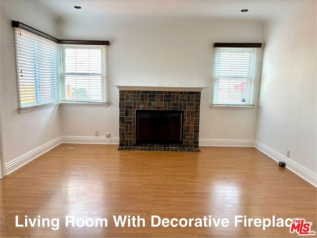 unfurnished living room with a healthy amount of sunlight, a tiled fireplace, and wood-type flooring