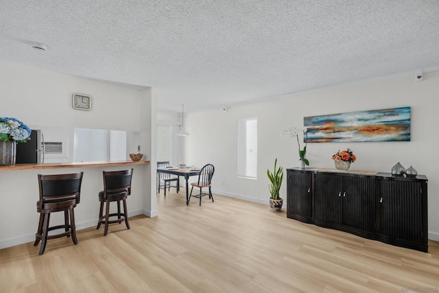 interior space featuring a kitchen breakfast bar, stainless steel fridge, a textured ceiling, and light hardwood / wood-style flooring