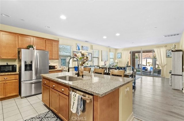 kitchen featuring light tile patterned floors, an island with sink, stainless steel appliances, light stone counters, and sink