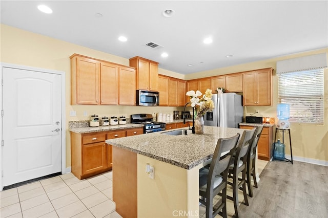 kitchen featuring an island with sink, appliances with stainless steel finishes, a kitchen breakfast bar, light stone countertops, and sink