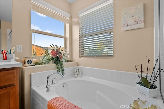 bathroom featuring plenty of natural light, tiled tub, and vanity