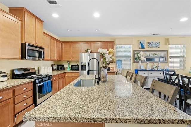 kitchen with a kitchen bar, light stone counters, stainless steel appliances, and a kitchen island with sink