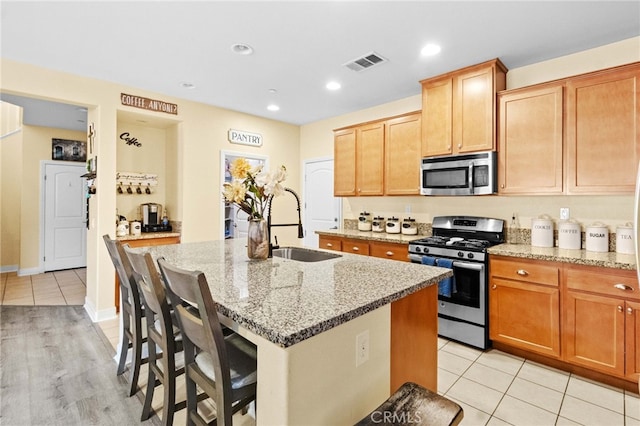 kitchen featuring a breakfast bar, a kitchen island with sink, light stone countertops, appliances with stainless steel finishes, and light tile patterned floors