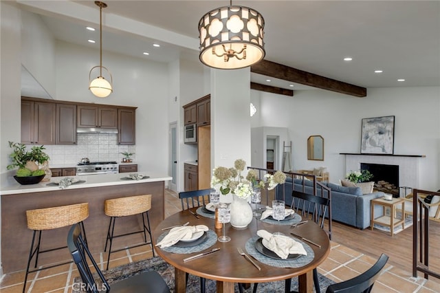 dining room with a towering ceiling, a brick fireplace, an inviting chandelier, light tile patterned flooring, and beamed ceiling