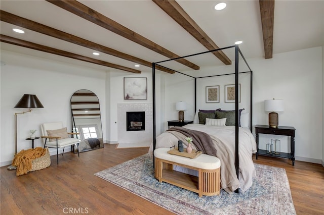 bedroom featuring wood-type flooring, a tile fireplace, and beamed ceiling