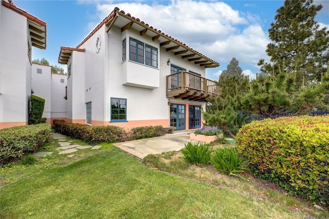 rear view of house with a balcony, a patio, and a yard