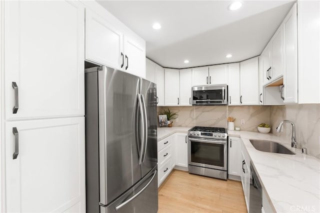 kitchen with sink, appliances with stainless steel finishes, tasteful backsplash, light stone countertops, and white cabinets