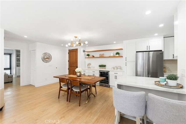 dining area featuring wine cooler, a notable chandelier, and light hardwood / wood-style flooring