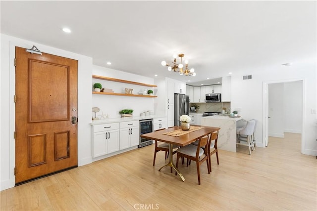 dining room featuring an inviting chandelier, wine cooler, and light wood-type flooring