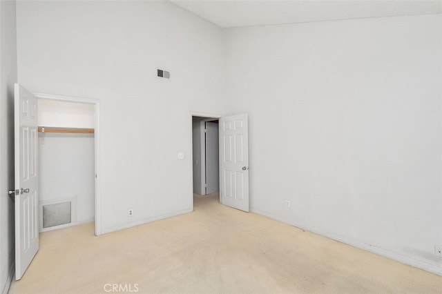 unfurnished bedroom with a high ceiling, light colored carpet, and a closet