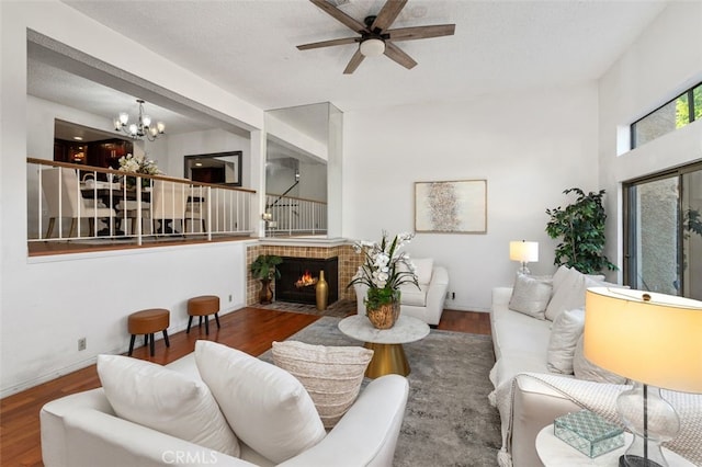 living room with hardwood / wood-style flooring, ceiling fan with notable chandelier, and a brick fireplace