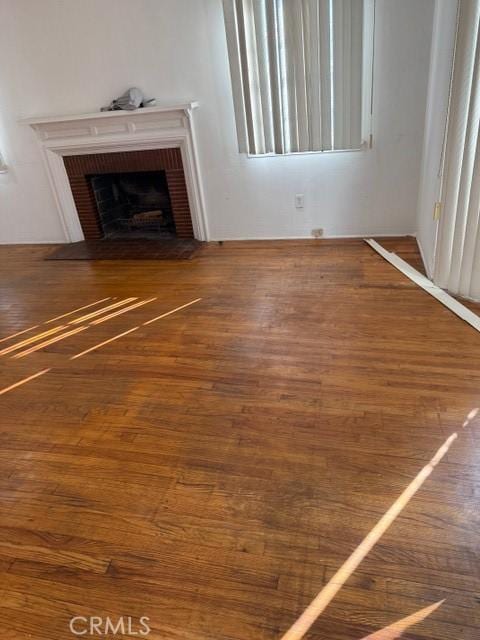 unfurnished living room featuring wood-type flooring and a brick fireplace