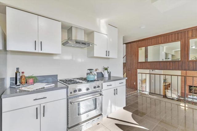 kitchen featuring stainless steel stove, wood walls, ventilation hood, white cabinets, and dark tile patterned floors