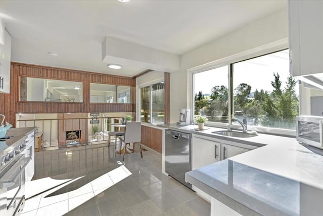 kitchen featuring sink, light tile patterned floors, appliances with stainless steel finishes, wooden walls, and white cabinets