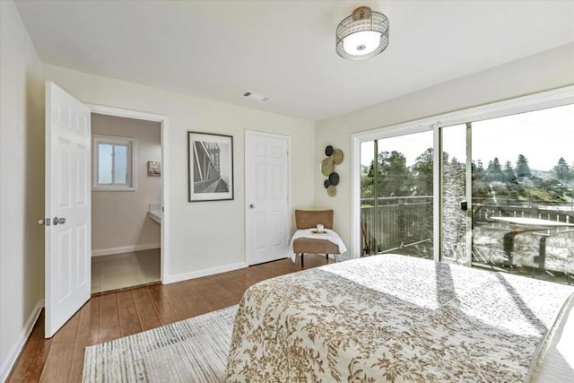 bedroom with ensuite bath, dark hardwood / wood-style floors, and access to outside