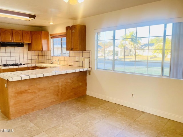 kitchen with kitchen peninsula, tile countertops, backsplash, plenty of natural light, and sink