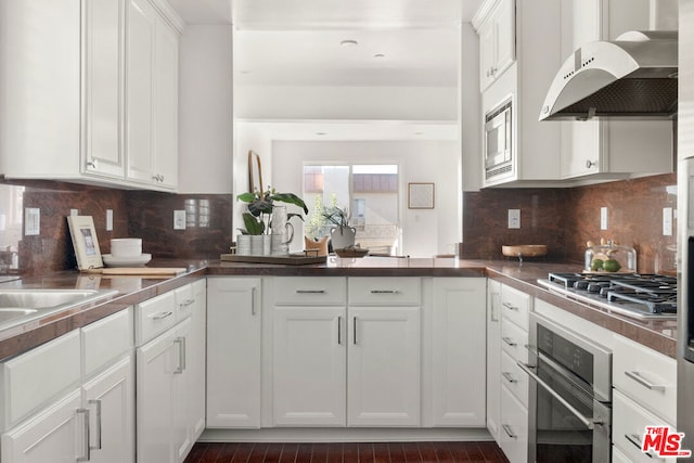 kitchen with kitchen peninsula, range hood, stainless steel appliances, tasteful backsplash, and white cabinetry