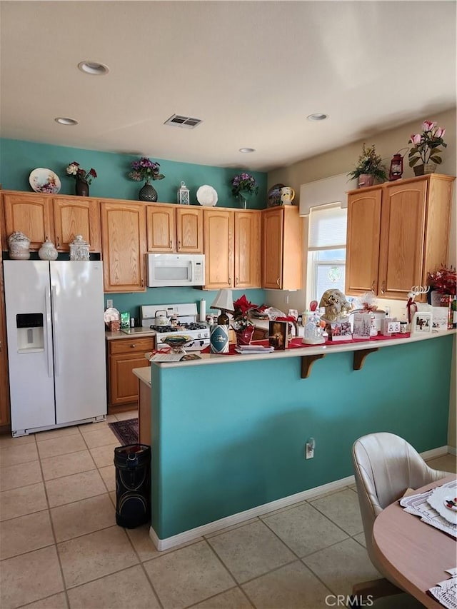 kitchen featuring white appliances, a kitchen bar, kitchen peninsula, and light tile patterned floors