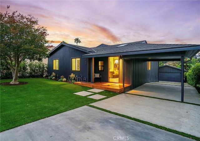 back house at dusk with a yard, a carport, an outdoor structure, and a garage