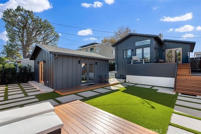 rear view of property with a deck, a lawn, and an outdoor structure