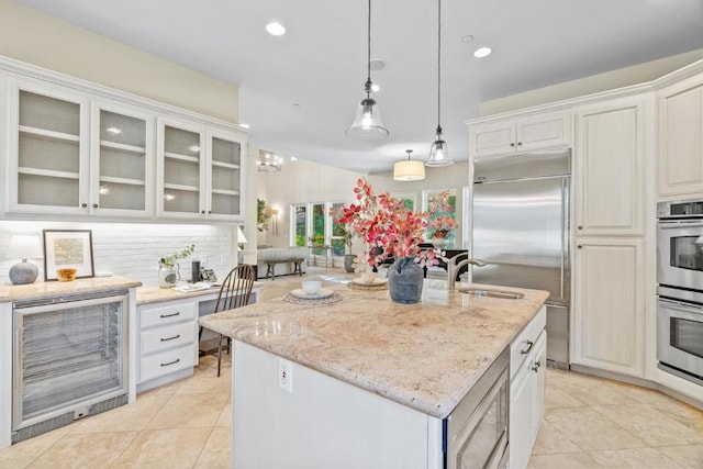 kitchen with built in appliances, pendant lighting, a center island with sink, wine cooler, and white cabinets