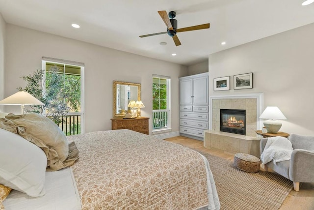 bedroom with ceiling fan, light hardwood / wood-style floors, multiple windows, and a fireplace