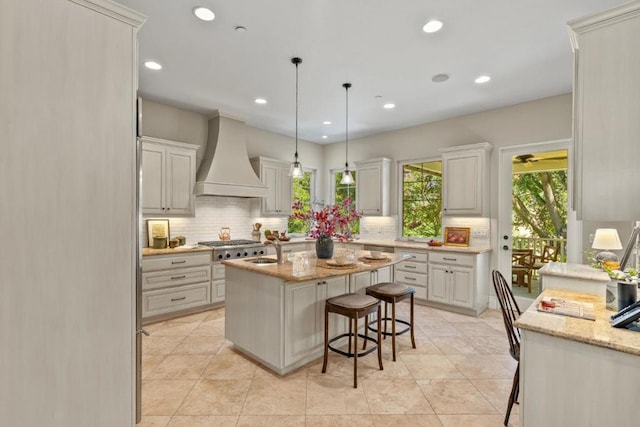 kitchen with an island with sink, custom range hood, a breakfast bar, light stone counters, and white cabinets