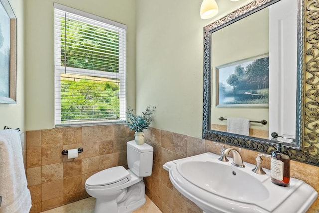 bathroom with toilet, tile walls, sink, and a healthy amount of sunlight