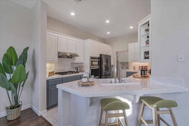 kitchen with appliances with stainless steel finishes, a breakfast bar, white cabinetry, sink, and kitchen peninsula