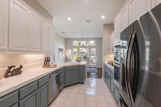 kitchen featuring gray cabinets, stainless steel appliances, white cabinets, light tile patterned flooring, and decorative light fixtures