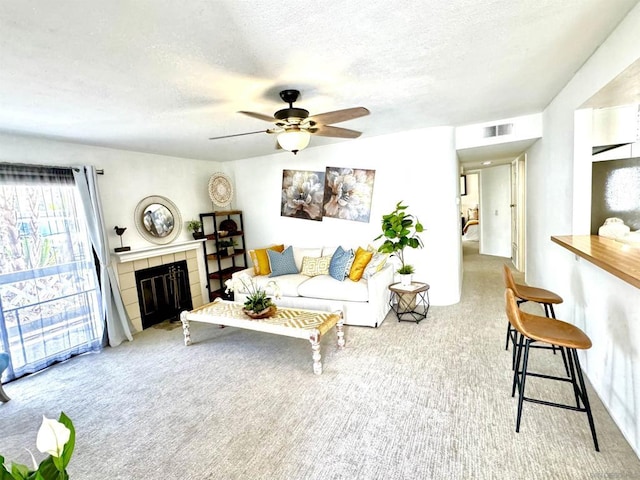 living room featuring ceiling fan, a tiled fireplace, light carpet, and a textured ceiling