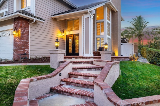 exterior entry at dusk with french doors, a lawn, and a garage