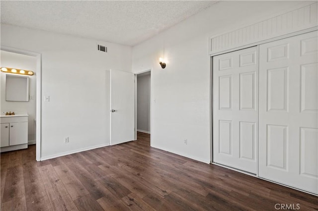 unfurnished bedroom with sink, a textured ceiling, connected bathroom, a closet, and dark hardwood / wood-style flooring