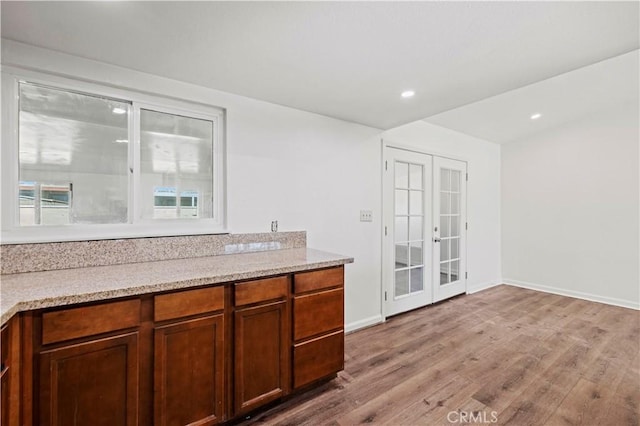 bar featuring light stone counters, french doors, and light hardwood / wood-style floors