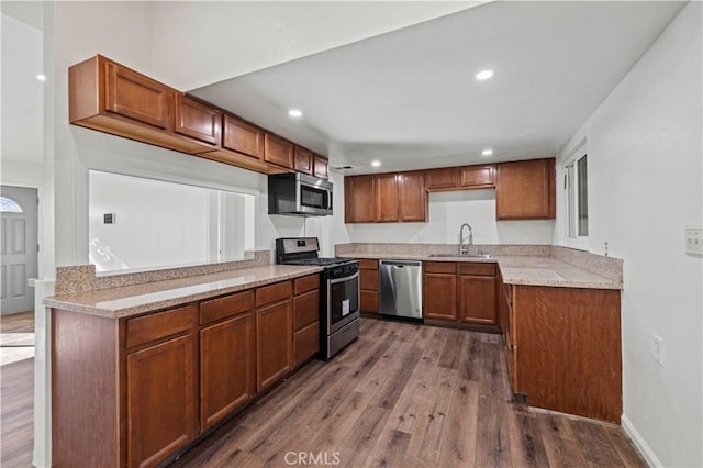 kitchen with appliances with stainless steel finishes, kitchen peninsula, dark hardwood / wood-style flooring, light stone counters, and sink