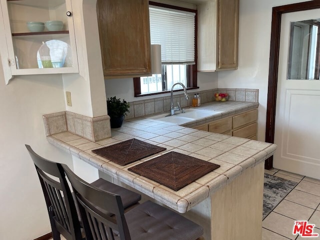 kitchen featuring a breakfast bar, tile countertops, sink, light tile patterned floors, and kitchen peninsula