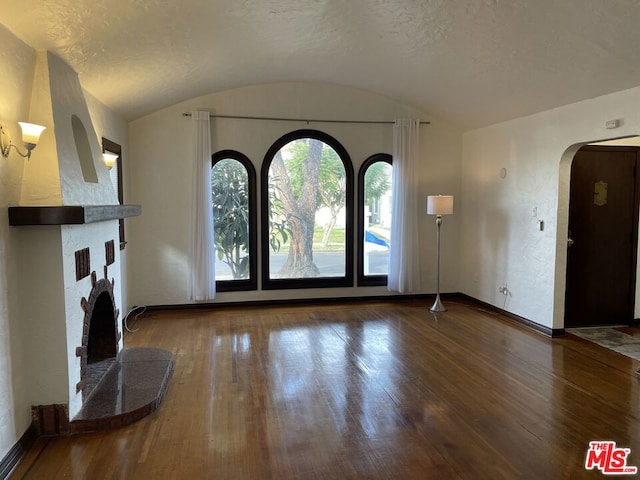 entryway with dark wood-type flooring, a fireplace, vaulted ceiling, and a textured ceiling