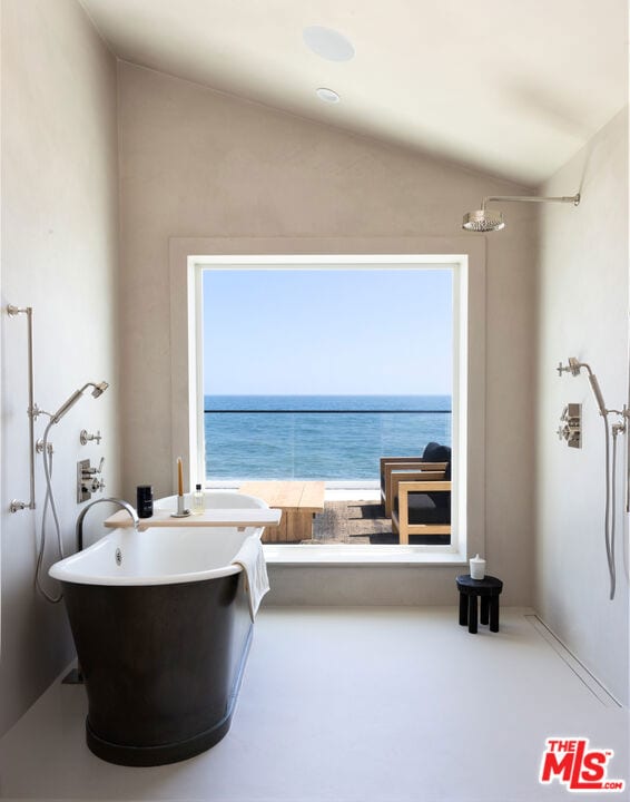 bathroom with a water view, vaulted ceiling, and a tub