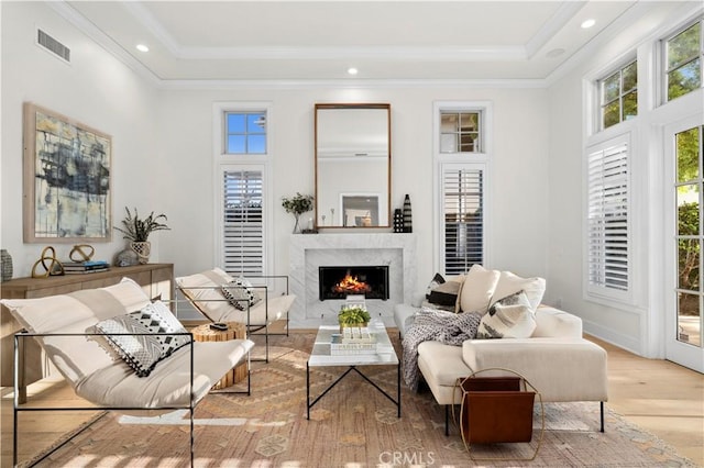 sitting room featuring a high end fireplace, a raised ceiling, plenty of natural light, and light hardwood / wood-style flooring