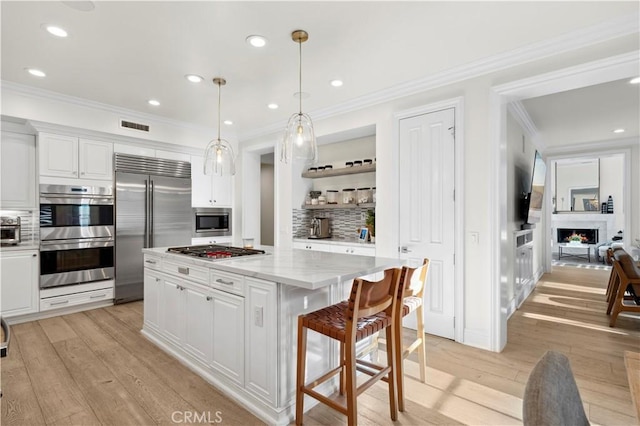 kitchen featuring built in appliances, a center island, hanging light fixtures, and white cabinetry