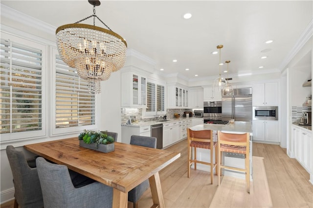 dining space with sink, ornamental molding, a chandelier, and light wood-type flooring