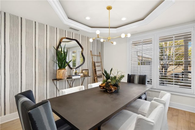 dining space with ornamental molding, a raised ceiling, light wood-type flooring, and a notable chandelier