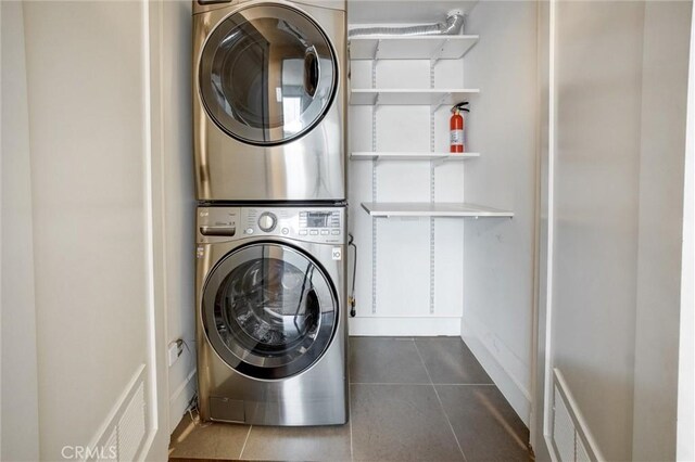 laundry room with stacked washer / drying machine and dark tile patterned flooring