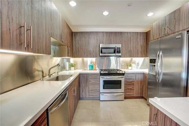 kitchen with brown cabinets, light tile patterned floors, light countertops, appliances with stainless steel finishes, and a sink