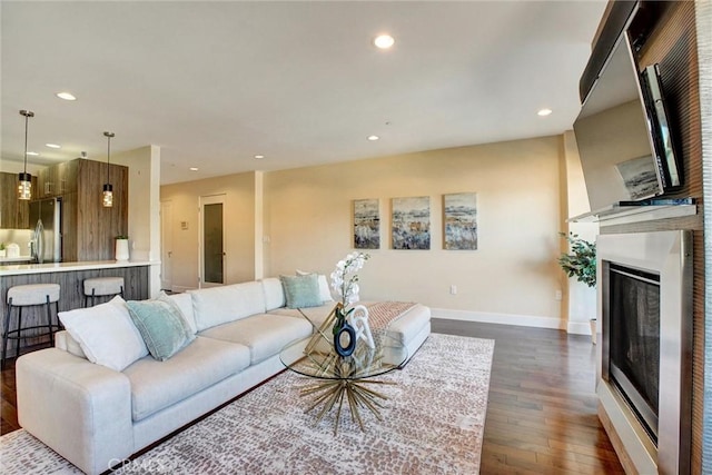 living area featuring a glass covered fireplace, dark wood finished floors, baseboards, and recessed lighting