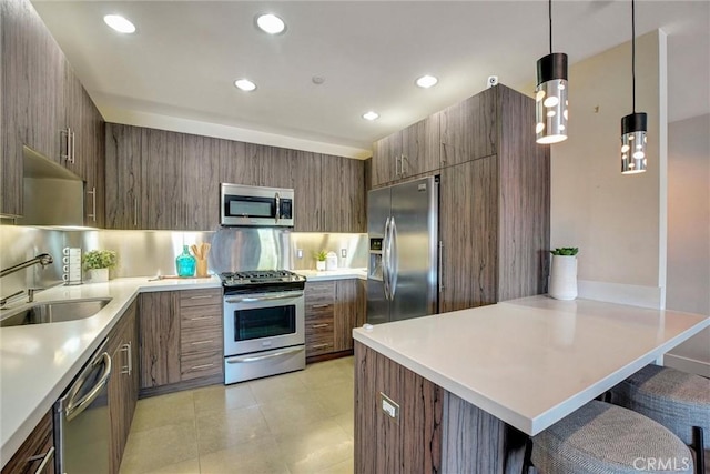 kitchen featuring stainless steel appliances, a sink, light countertops, modern cabinets, and a kitchen bar