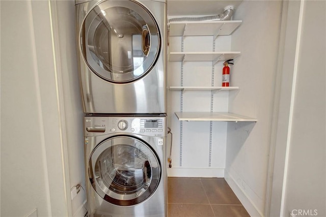 clothes washing area with tile patterned flooring, baseboards, stacked washing maching and dryer, and laundry area