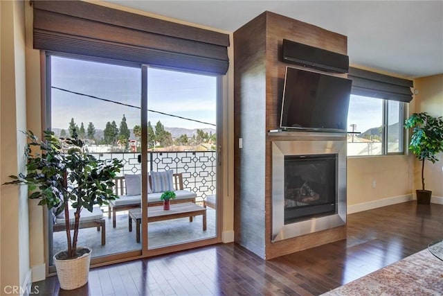 living area with dark wood-type flooring, a glass covered fireplace, and baseboards